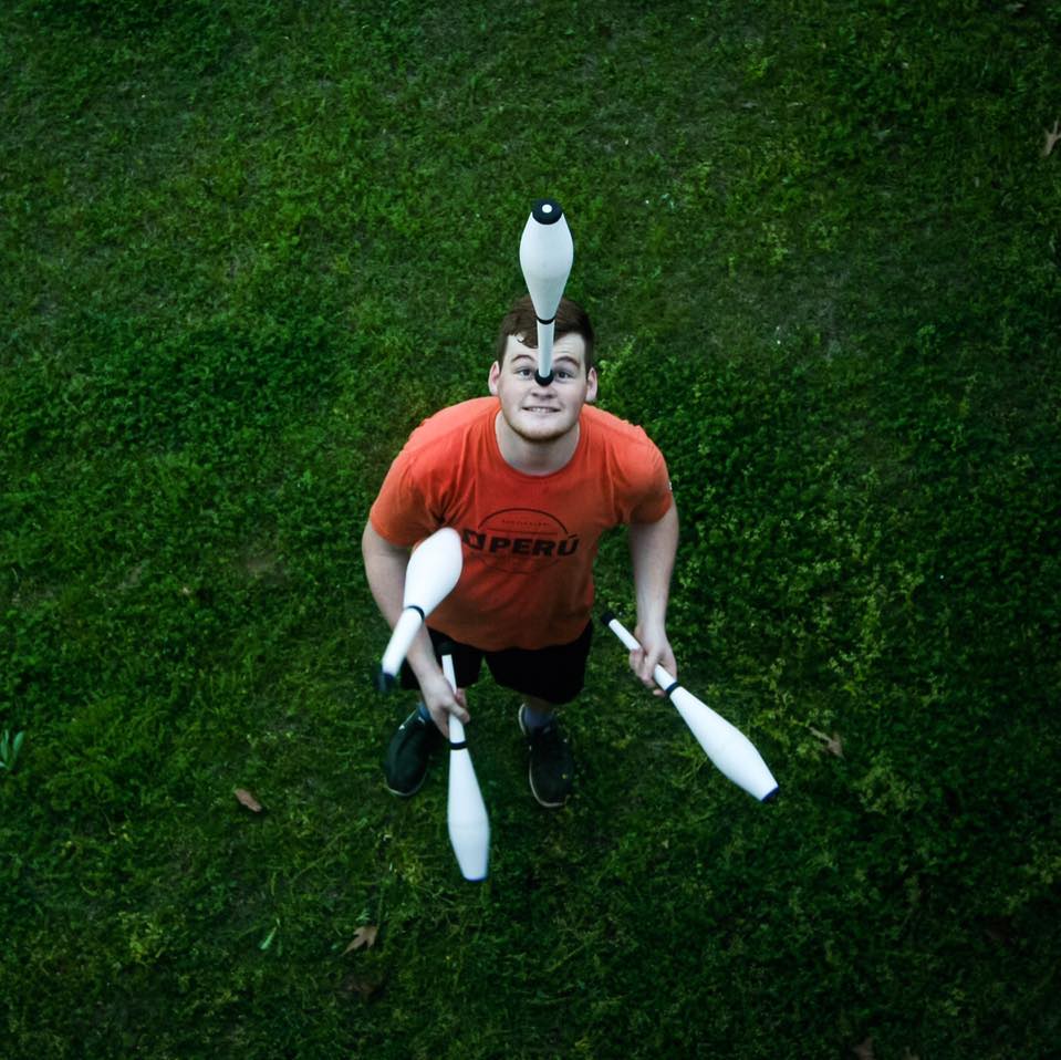 Spencer in orange shirt juggling 4 clubs