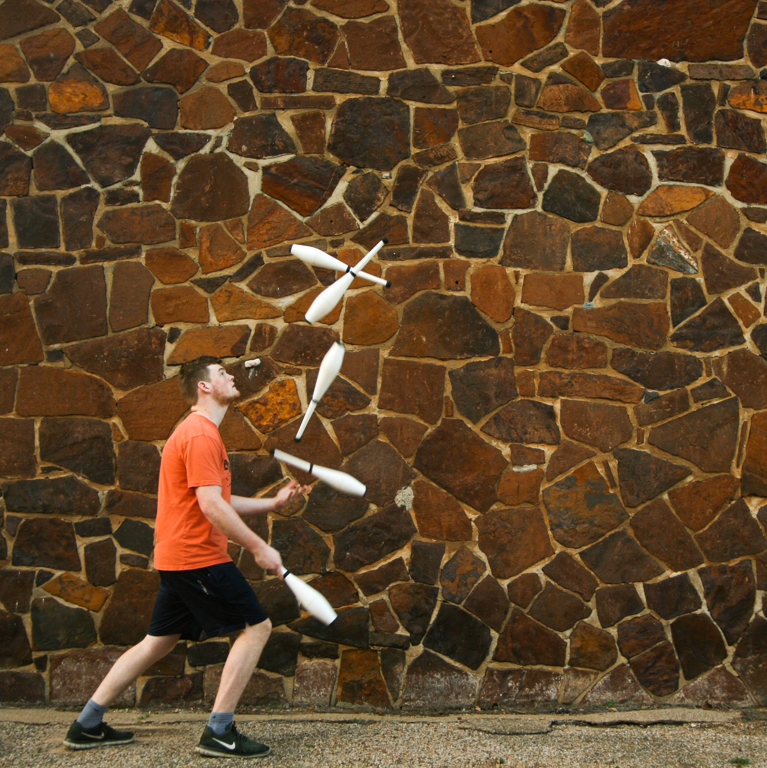 Spencer Androli juggling clubs next to stone wall